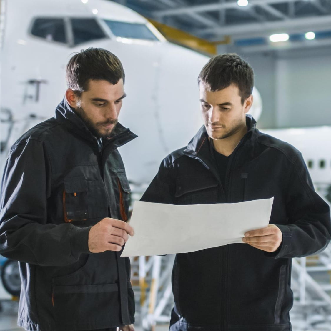 Two aircraft maintenance technicians reviewing a document in a hangar